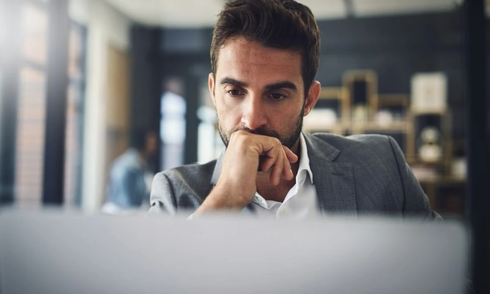 Un homme en costume, concentré devant son ordinateur, semble réfléchir à une décision importante.