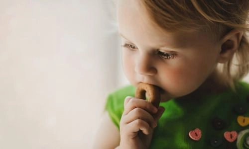 Un jeune enfant mange tranquillement un petit biscuit en regardant dans le vide.