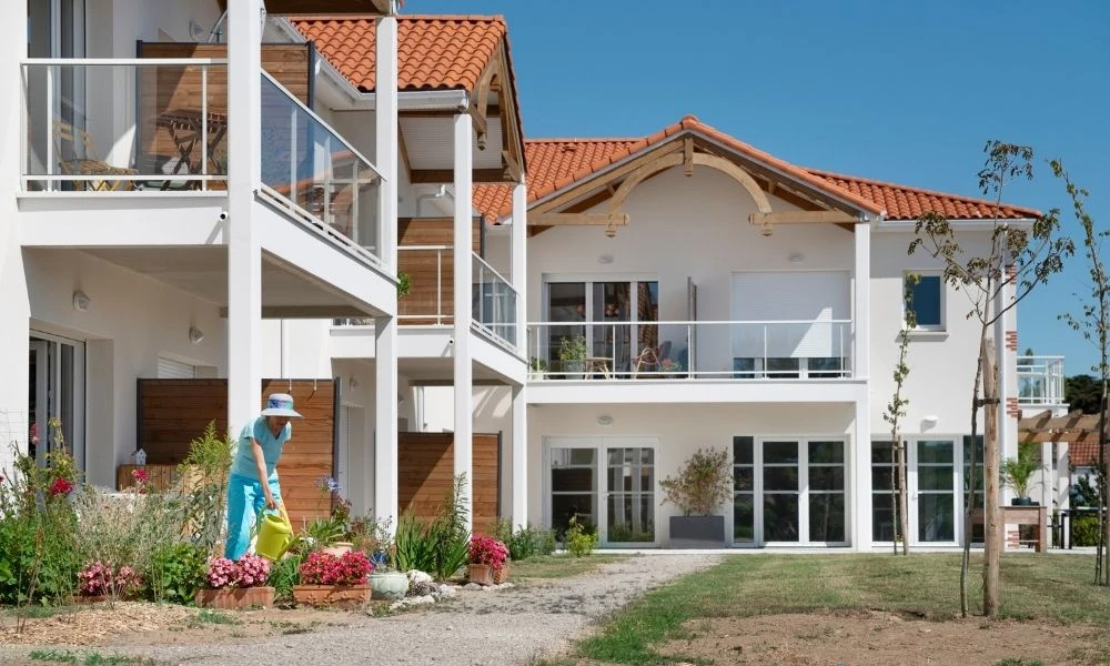 Le visuel montre une résidence autonomie Marpa lumineuse avec un jardin fleuri et des balcons accueillants.