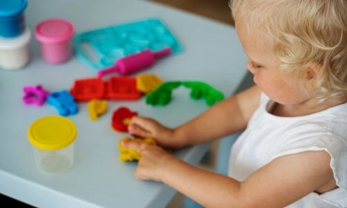 Un tout-petit joue avec de la pâte à modeler colorée sur une table, concentré sur ses créations.