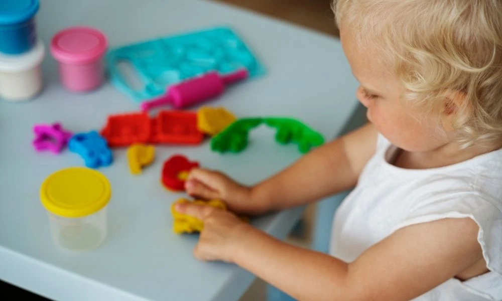Un tout-petit joue avec de la pâte à modeler colorée sur une table, concentré sur ses créations.