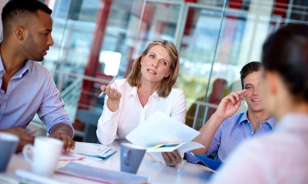 Une équipe de professionnels échange autour de documents lors d’une réunion de travail, dans un environnement collaboratif.