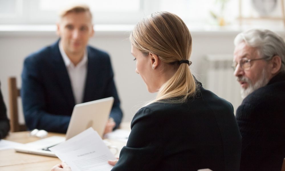 Une réunion professionnelle où plusieurs personnes échangent autour de documents et d’un ordinateur portable, dans un cadre de travail.