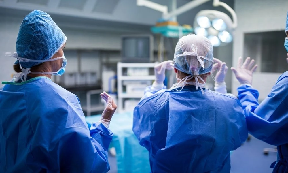 Des professionnels de santé en tenue stérile travaillent ensemble dans un bloc opératoire, illustrant l’hygiène et la coordination des équipes.