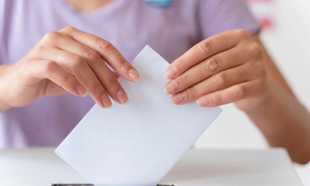Mains de femme qui insèrent un bulletin de vote dans une urne. L’enveloppe est blanche.