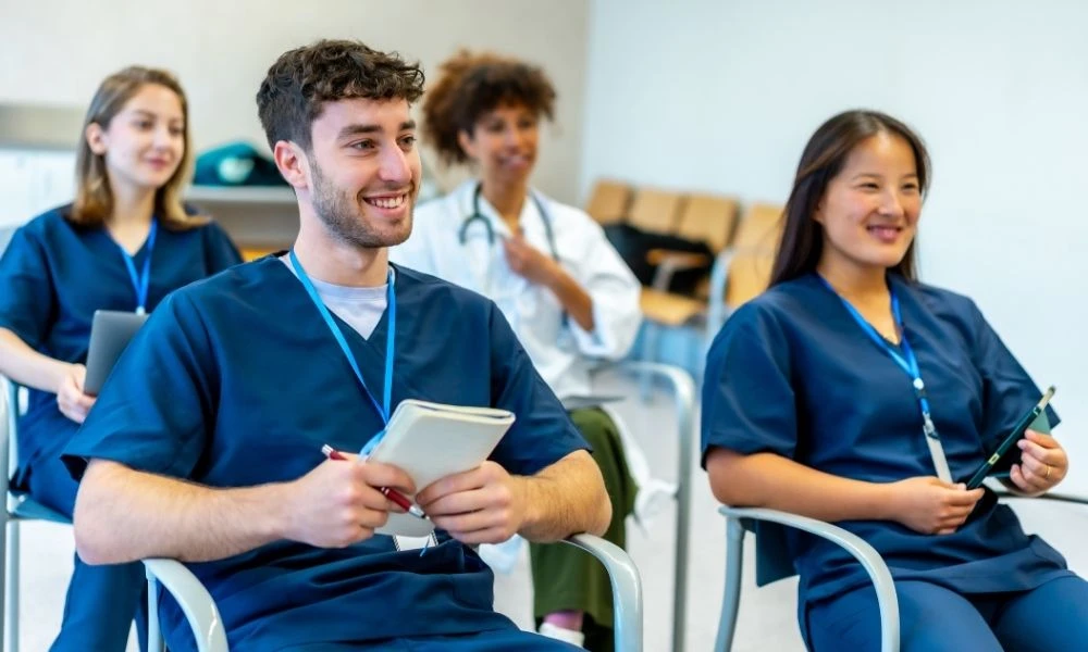 Un groupe de professionnels de santé, en tenue médicale, assis en formation ou réunion, écoutant attentivement avec des supports de prise de notes.