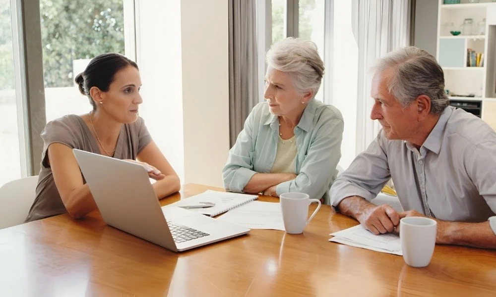 Trois personnes sont réunies autour d’une table, échangeant calmement avec une professionnelle devant un ordinateur portable, dans un cadre lumineux et rassurant.