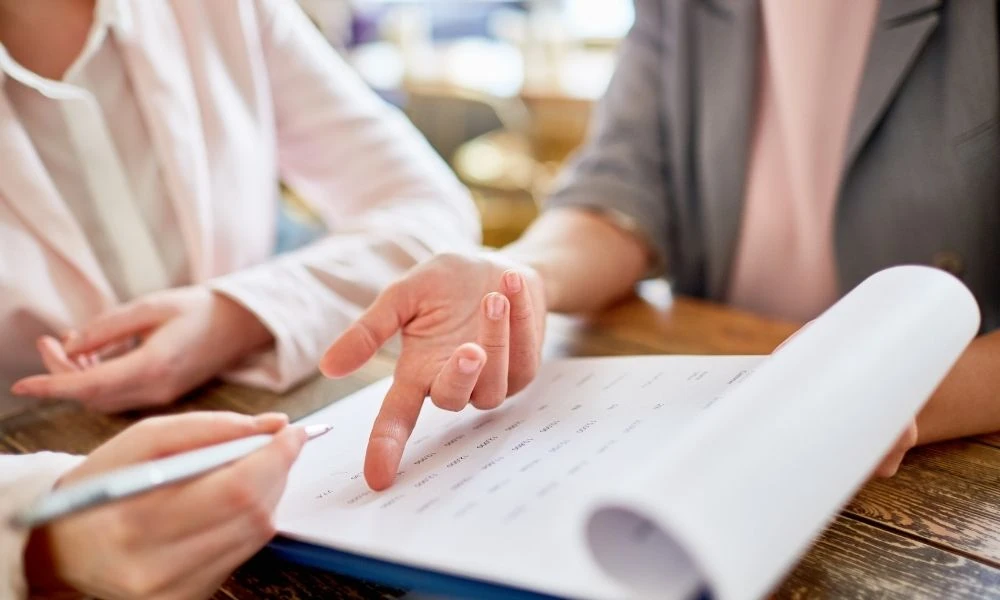 Deux personnes examinent ensemble un document, l’une pointant une section tandis que l’autre prend des notes.