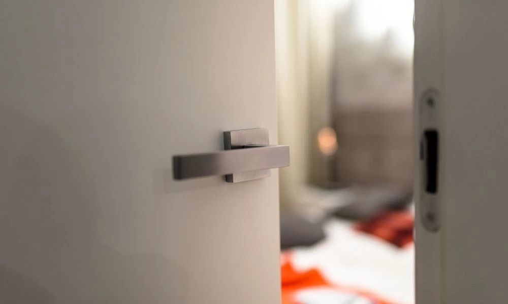 Une porte blanche avec une poignée moderne en métal est entrouverte, révélant un intérieur flou.