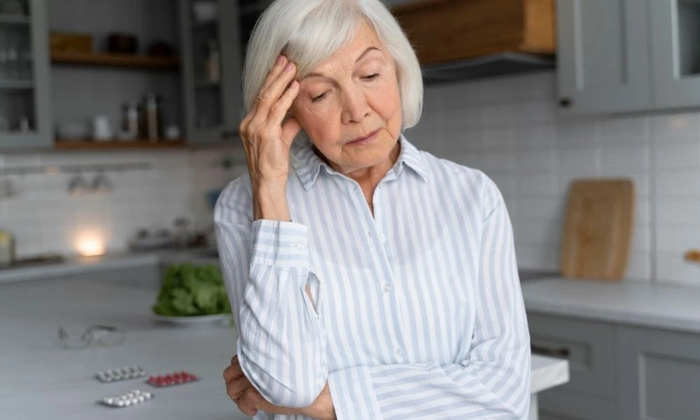 Dame âgée atteinte d'Alzheimer et qui se tient la tête dans sa cuisine.
