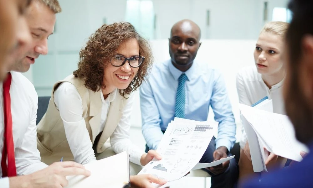 Une personne en tenue professionnelle tient plusieurs dossiers et documents dans les mains.