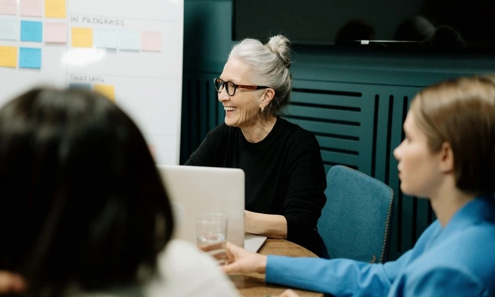 Une femme souriante participe à une réunion autour d’une table avec ses collègues.