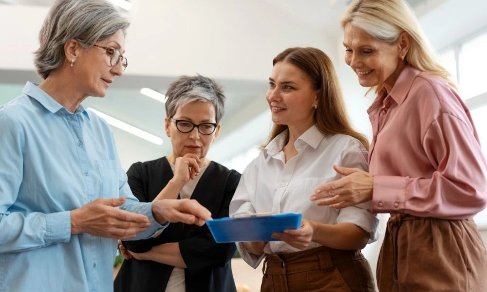 Quatre femmes, dont des professionnelles et une personne âgée, échangent autour d’un document dans un cadre de travail collaboratif.