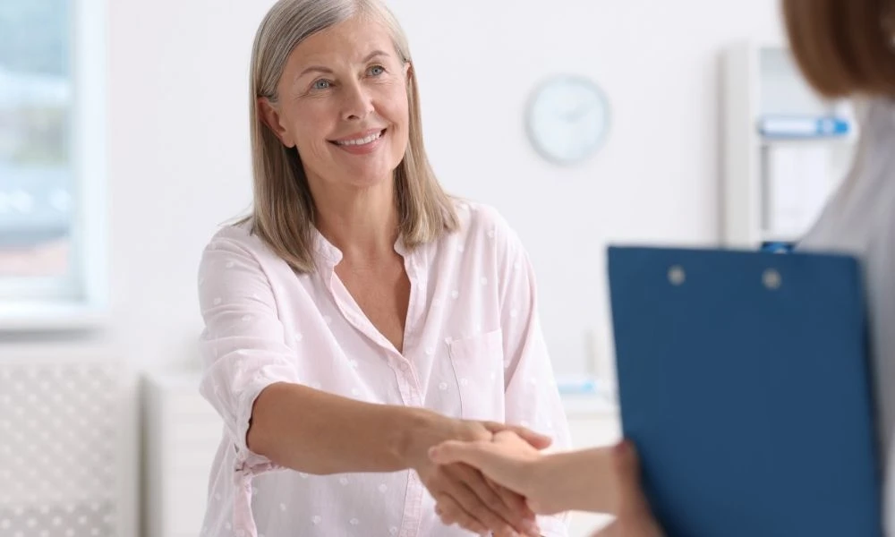 Une femme souriante serre la main d’un professionnel dans un environnement médical, évoquant un échange bienveillant et professionnel.