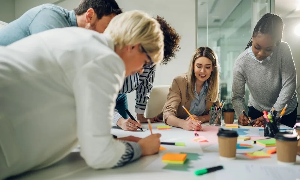 Un groupe de professionnels collabore activement autour d’une table couverte de notes et de documents.
