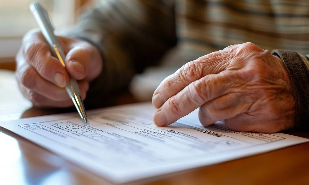 Une personne âgée tient un stylo et complète un document sur une table.
