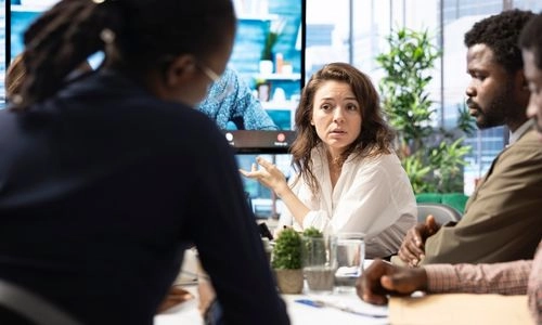 Une femme s'exprime avec conviction lors d'une réunion d'équipe, entourée de collègues attentifs autour d'une table de travail.