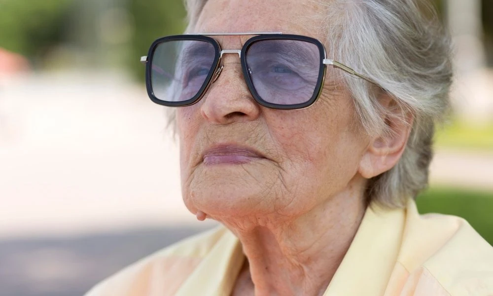 Portrait d'une dame âgée portant de grandes lunettes teintées et regardant au loin avec bienveillance.