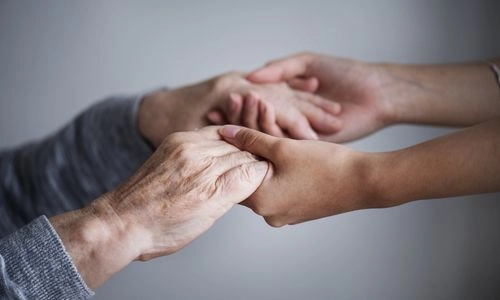 Deux personnes se tiennent les mains avec bienveillance, illustrant le soutien et la confiance.