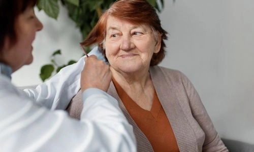 Une aide-soignante coiffe une dame âgée souriante.