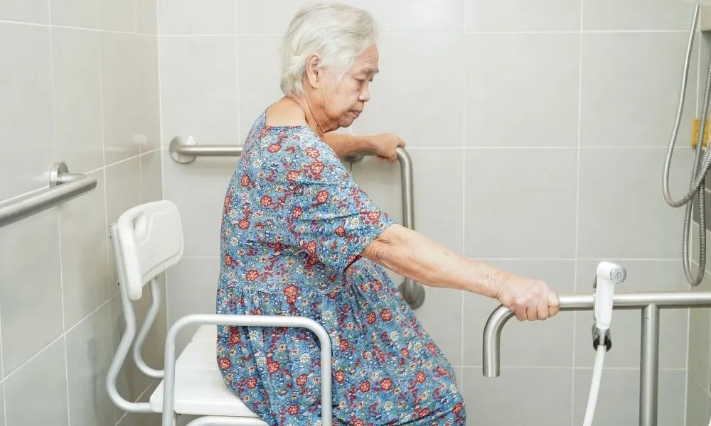 Une personne âgée utilise des barres d’appui dans une salle de bain adaptée pour faciliter sa mobilité et sa sécurité.