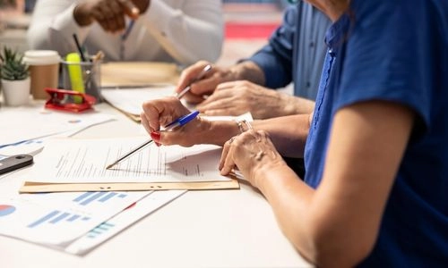 Trois personnes autour d'une table analysent ensemble des documents et graphiques, stylos à la main.