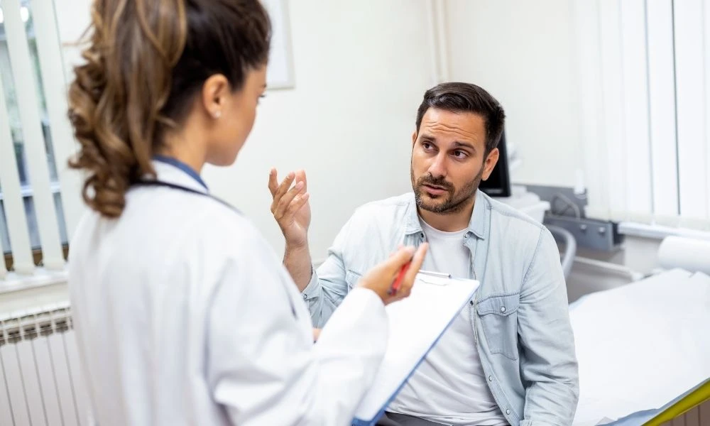 Une femme médecin discute avec un patient assis dans une salle de consultation médicale.