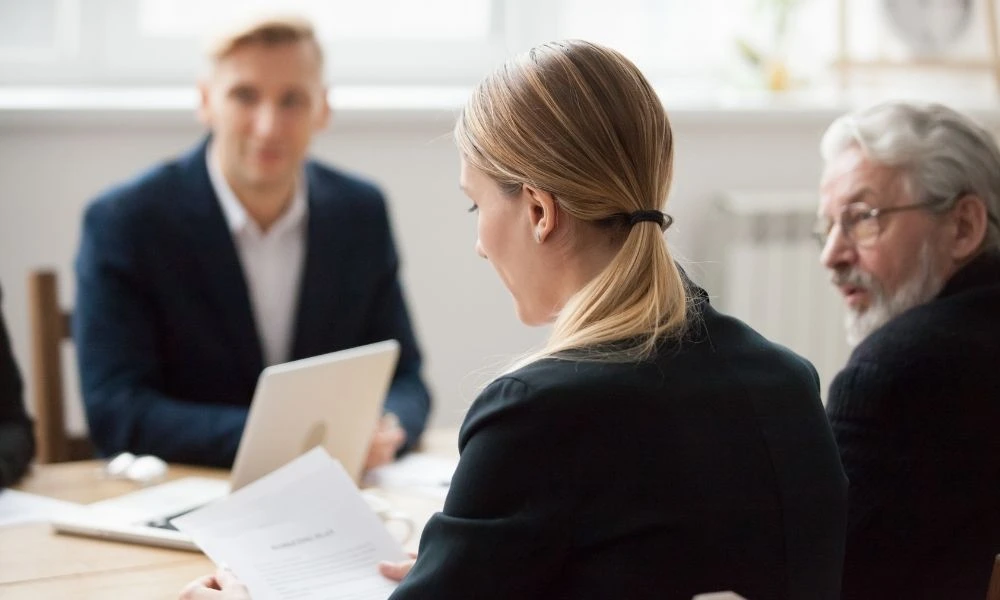 Une réunion professionnelle où plusieurs personnes échangent autour de documents et d’un ordinateur portable, dans un cadre de travail.