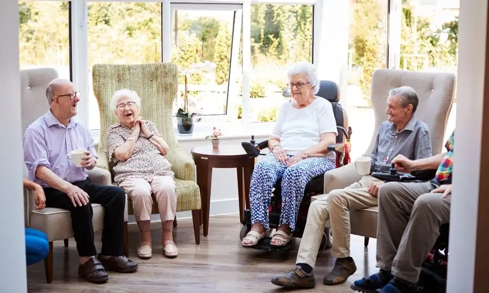Un groupe de résidents d’EHPAD partage un moment convivial en discutant et en riant dans un salon lumineux.