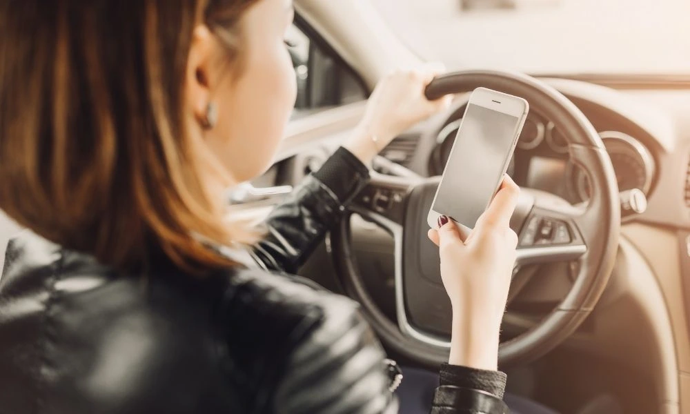 Une personne conduit en tenant son volant d’une main et utilise son téléphone portable de l’autre, ce qui illustre une situation de distraction au volant.