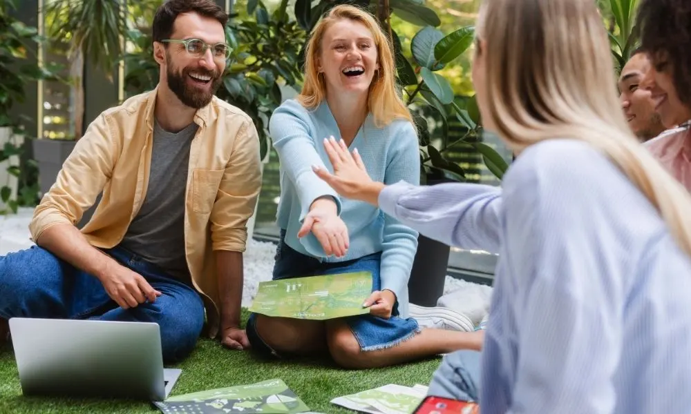 Un groupe de personnes assises en cercle, souriant et échangeant des poignées de main dans une ambiance collaborative et joyeuse.