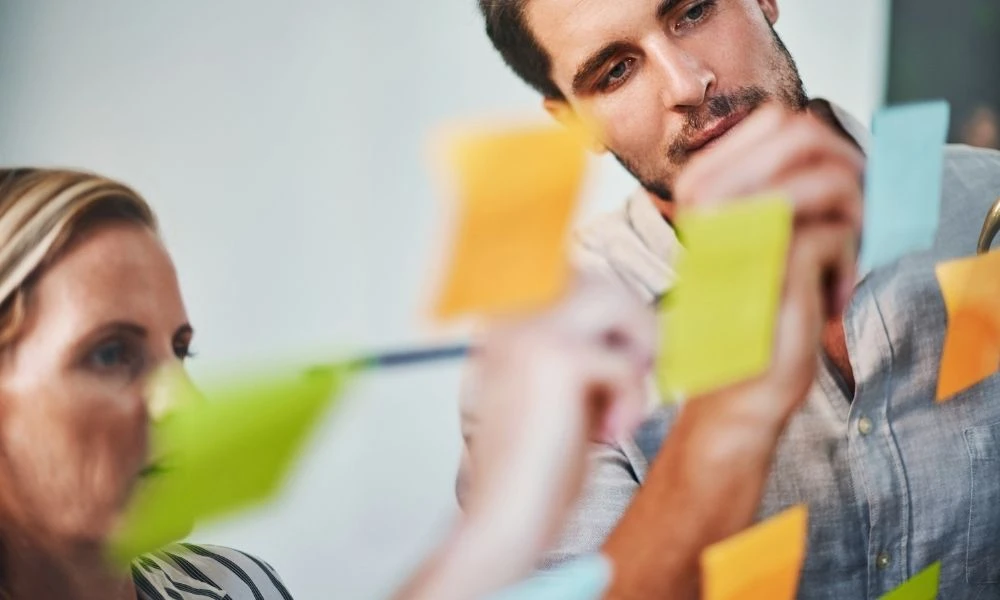 Deux personnes travaillent ensemble, tenant des post-it colorés pour planifier ou organiser un projet.
