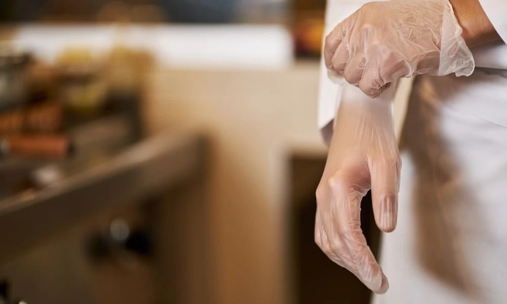 Une personne enfile un gant de latex dans une cuisine professionnelle évoquant une situation nécessitant hygiène et précision.
