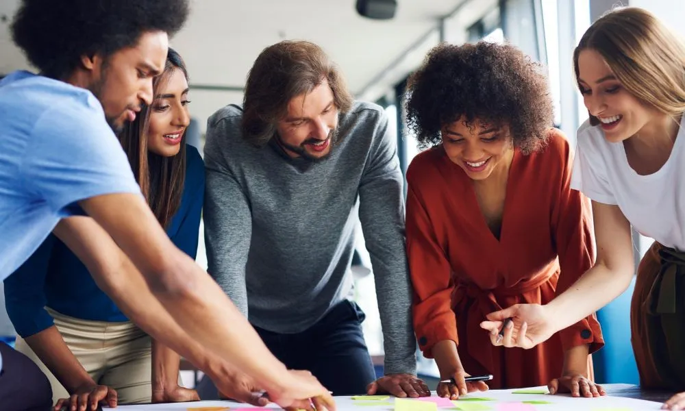 Un groupe diversifié de personnes travaille ensemble autour d'une table, discutant et collaborant avec enthousiasme.