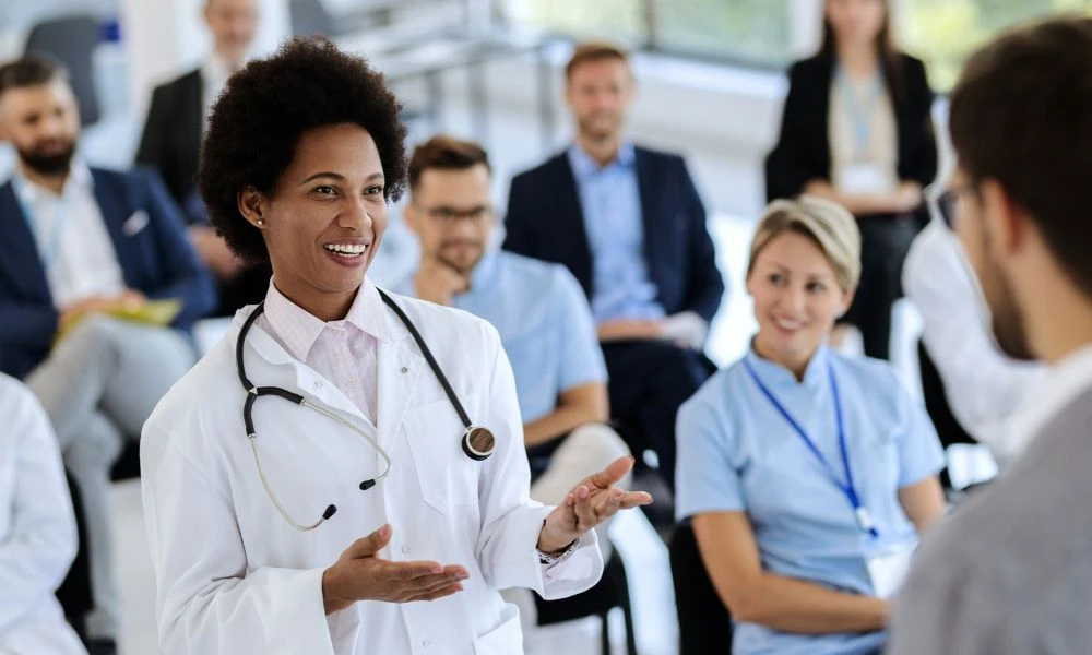 Un groupe de professionnels de santé en tenue médicale discute de manière concentrée autour d’une tablette, manifestement engagés dans une réunion de travail ou une discussion clinique collaborative.