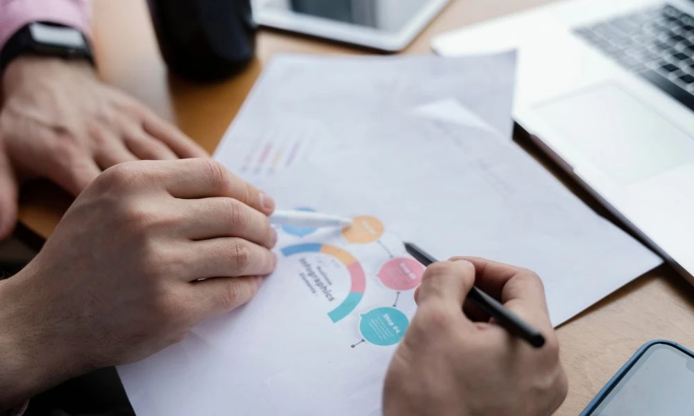 Deux personnes analysent un document contenant un diagramme de processus, avec un ordinateur portable en arrière-plan.