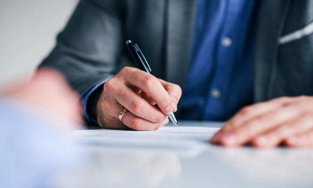 Un homme en costume signe un document avec un stylo sur un bureau