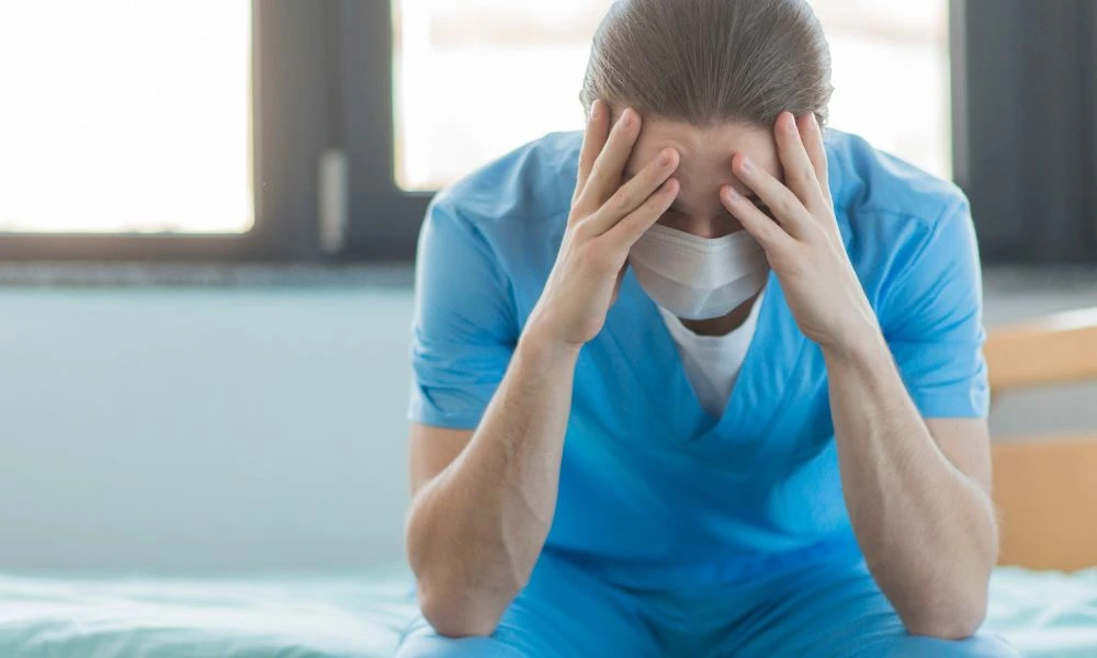 Un professionnel de santé épuisé et stressé est assis et tient la tête entre les mains.