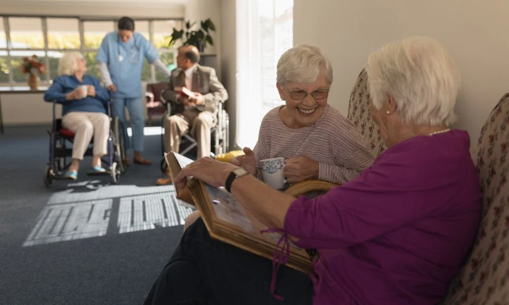 Cette image montre des personnes âgées dans une maison de retraite, en train de regarder des photos ensemble.