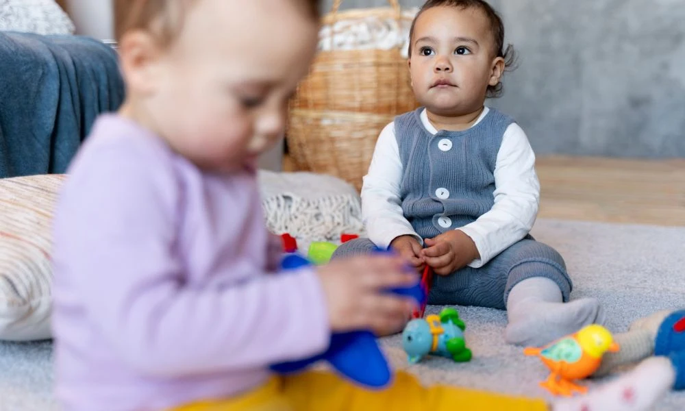 Cette image montre deux jeunes enfants en train de jouer dans une pièce avec des jouets colorés.L'ambiance est chaleureuse et typique d'un environnement adapté aux tout-petits, comme une crèche ou une salle de jeux.