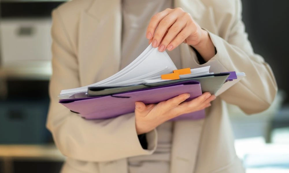 Personne en train de manipuler des documents. Elle tient des pochettes avec plusieurs documents à l'intérieur. L'image évoque une activité administrative liée à un contrôle ou une gestion de documents officiels.