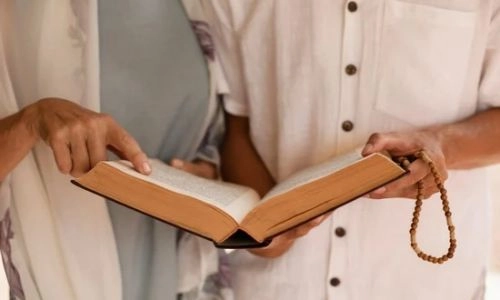 Cette image montre deux personnes en train de lire un texte religieux ou spirituel ensemble et l'une des personnes tient un chapelet en bois.