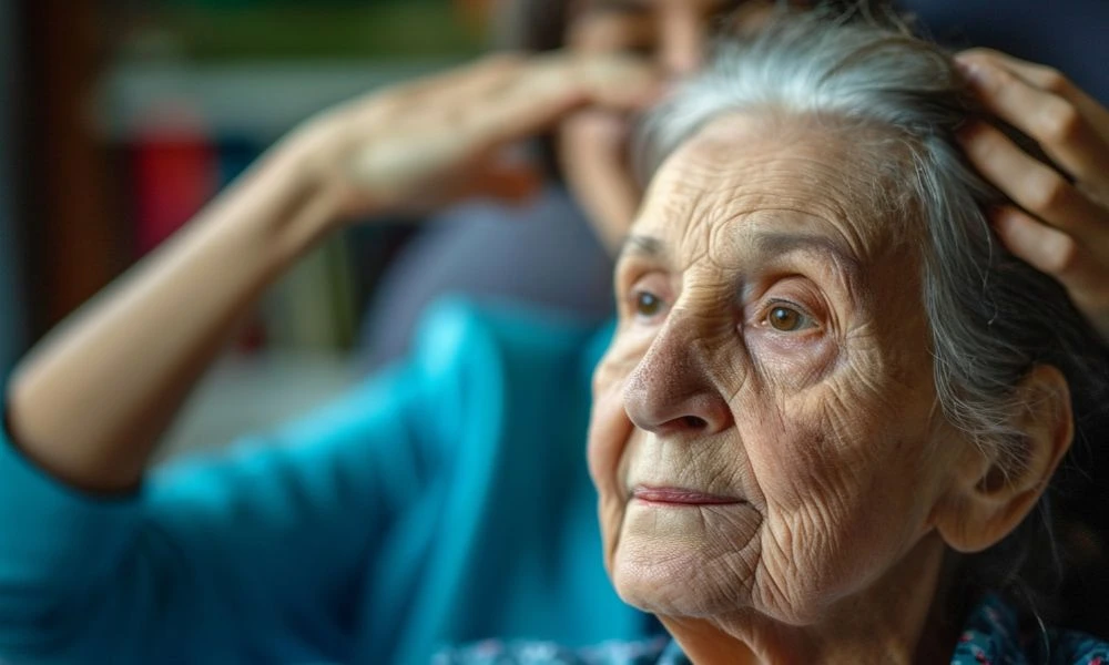 Dame âgée avec rides marquées et des cheveux gris. Derrière elle, une aide à domicile prend soin de ses cheveux en passant ses mains dans sa chevelure.