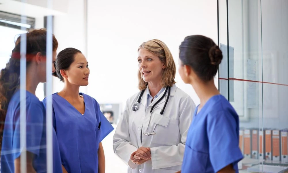 Une médecin échange avec trois soignantes dans un couloir d'établissement de santé.