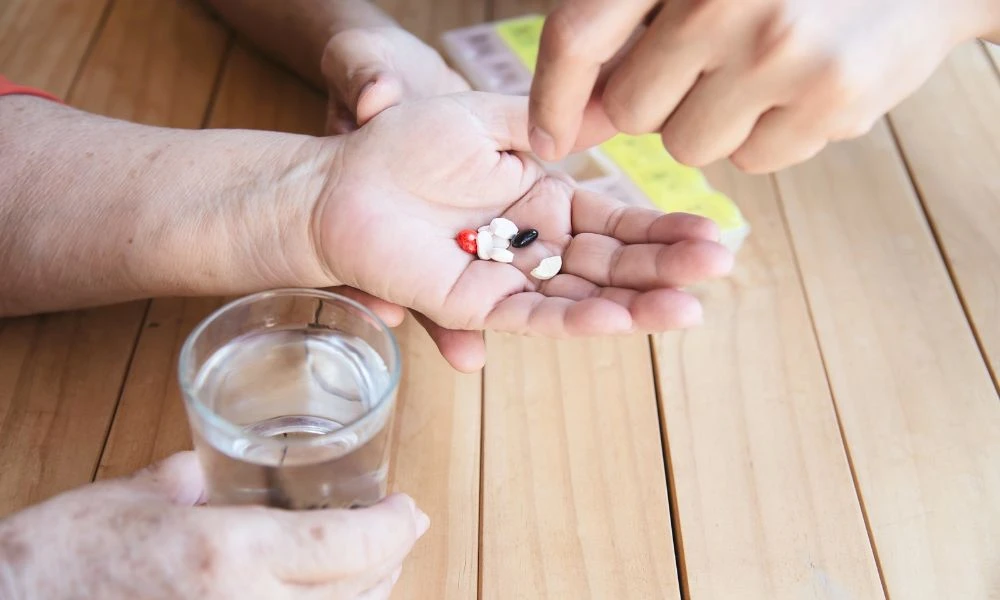 Une personne tient des médicaments dans sa main pendant qu’une autre l’aide à les préparer avec un verre d’eau.