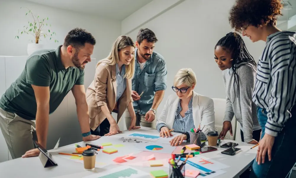 Un groupe de collègues collabore autour d’une table couverte de graphiques et de notes colorées.
