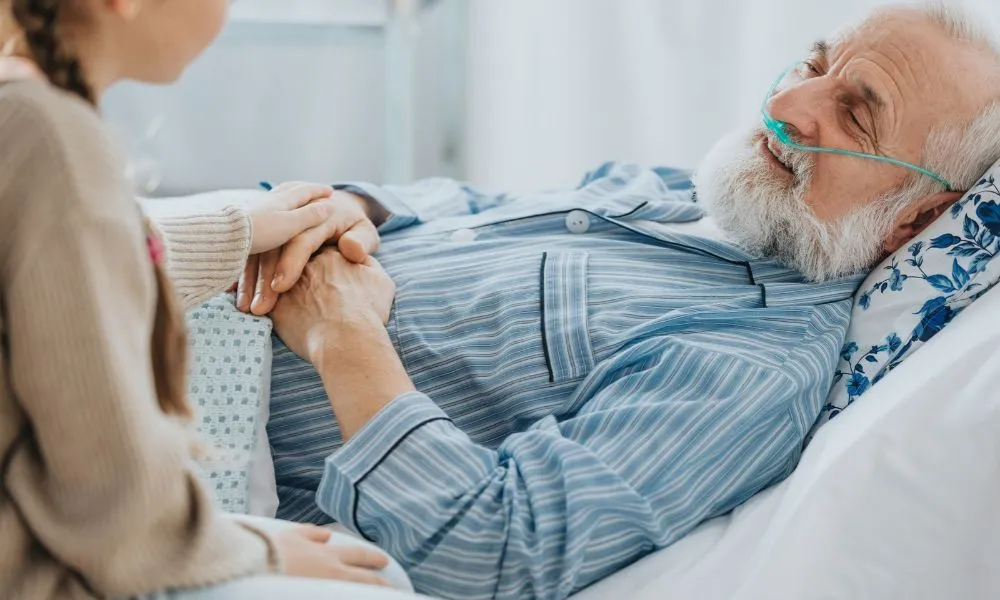 Un homme âgé hospitalisé reçoit la visite réconfortante d’un proche qui lui tient la main.