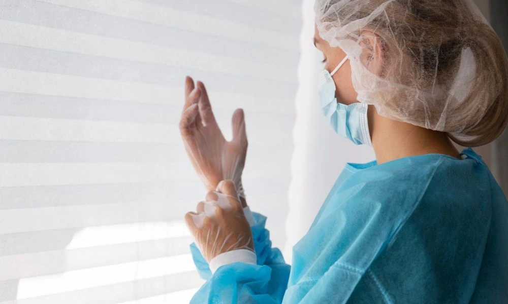 Une soignante en tenue de protection ajuste ses gants avant une intervention médicale.