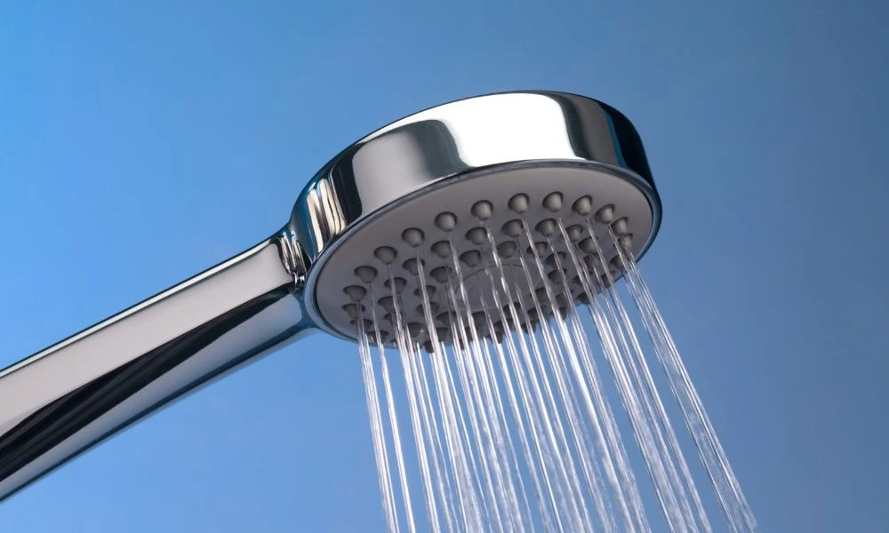 Un pommeau de douche métallique laisse couler un jet d’eau claire sur fond bleu.