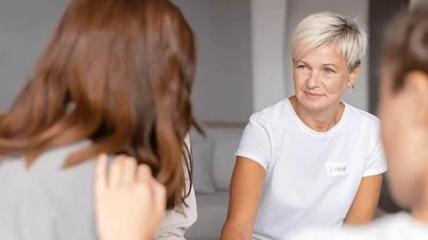 Une femme aux cheveux courts échange attentivement avec deux personnes dans un cadre convivial.